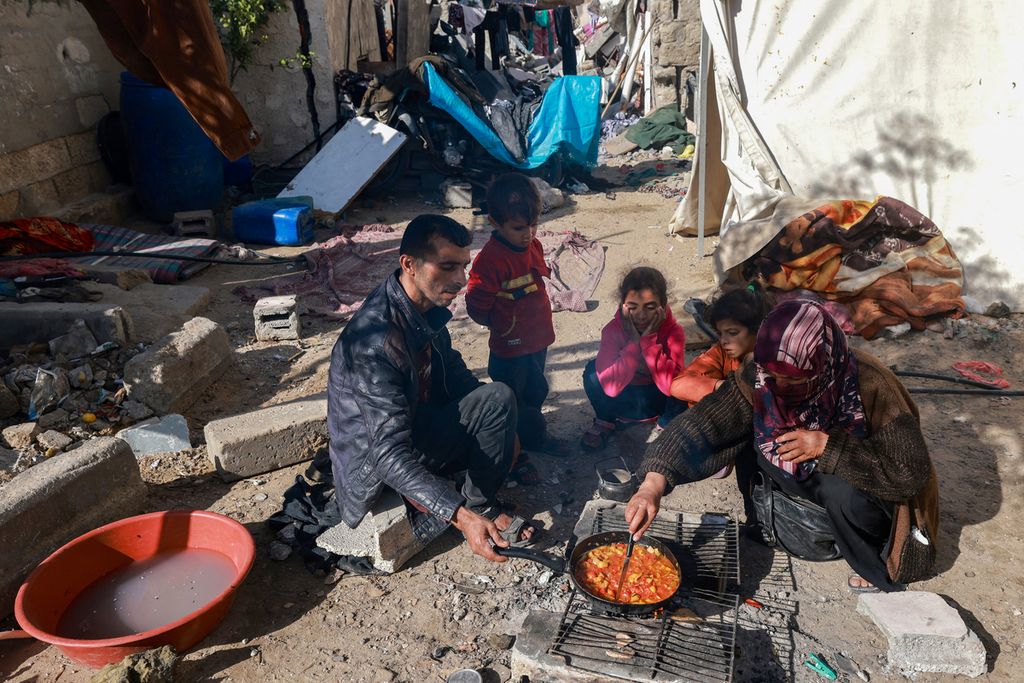  Keluarga Palestina memasak di luar rumah mereka yang rusak di Rafah di Jalur Gaza, Senin (11/12/2023).