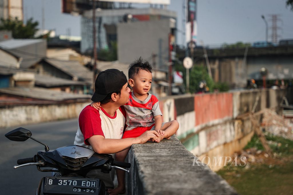 Orangtua menemani anaknya melihat aktivitas di bantaran Sungai Ciliwung di kawasan Duri Pulo, Jakarta Pusat, Kamis (3/8/2023). Bermain layangan dan sepak bola menjadi aktivitas favorit anak-anak di kawasan ini saat sore hari. Meski berisiko, kawasan permukiman yang padat membuat mereka bermain di bantaran sungai.