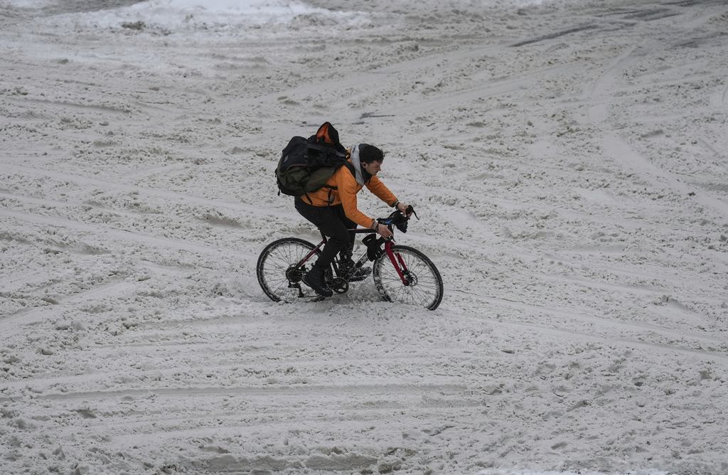Seorang pesepeda mengayuh sepedanya melintasi jalan Robson yang tertutup salju di pusat kota Vancouver, British Columbia, Kanada pada Jumat (23/12/2022).