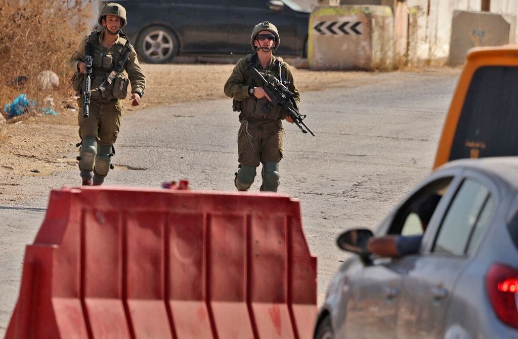 Kendaraan menunggu dalam antrean, sementara tentara Israel mendekat di sebuah pos pemeriksaan antara kota Nablus dan Desa Beit Furik, wilayah pendudukan Tepi Barat, Senin (24/10/2022).  