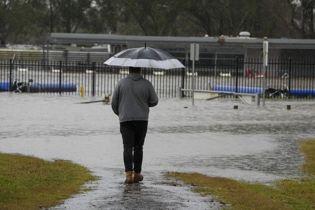 Seorang pria berdiri di dekat tempat olahraga yang terendam banjir di Camden, Sydney, Australia, Senin (4/7/2022). Sebanyak 32 ribu penduduk Sydney dan sekitarnya diperintahkan mengungsi atau bersiap untuk meninggalkan rumah mereka.