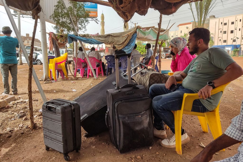 Seorang warga dengan beberapa kopernya menunggu bus untuk keluar dari Khartum, Sudan, 24 April 2023. Pertempuran antara dua faksi militer di Sudan memaksa ribuan orang meninggalkan Sudan. (Photo by AFP)