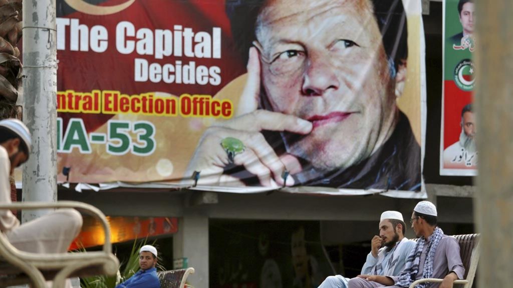 Warga Pakistan berbincang-bincang di dekat poster besar bergambar Pemimpin Partai Tehreek-e-Insaf (PTI) Imran Khan di sebuah pasar, di Islamabad, Sabtu (28/7/2018) silam. PTI berhasil memenangi pemilu Pakistan yang pemungutan suaranya berlangsung pada 25 Juli 2018.