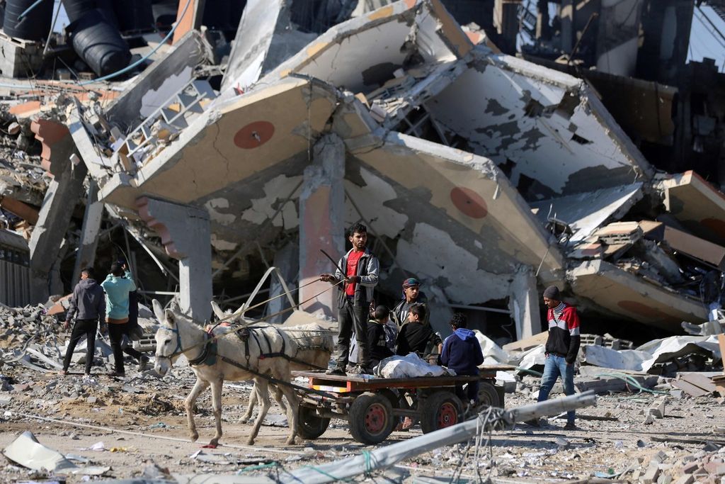 Kereta keledai melewati reruntuhan gedung di kamp pengungsi Al-Maghazi <i>refugee camp</i> di pusat Jalur Gaza, Selasa (16/1/2024), di tengah situasi perang Israel-Hamas.