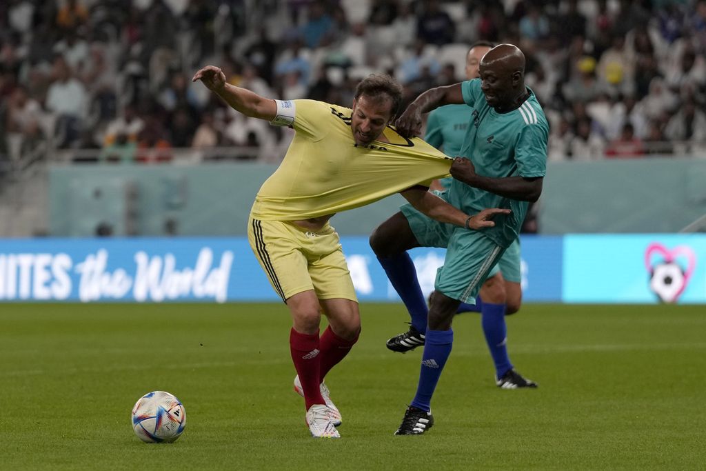 Kaus legenda sepak bola Italia, Alessandro Del Piero (kiri), ditarik oleh pemain lawan yang berlatar belakang pekerja pada laga sepak bola antara para pekerja dan para Legendaris FIFA di Stadion Al Thumama, Doha, Qatar, 12 Desember 2022. 