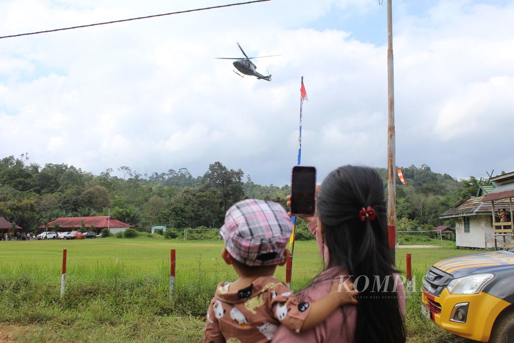 Warga Kinipan menggendong anaknya menyaksikan helikopter mendarat di halaman lapangan sepak bola di Desa Kinipan, Kecamatan Batang Kawa, Kabupaten Lamandau, Kalimantan Tengah, Sabtu (7/9/2024). Mereka antusias menyambut kedatangan menteri untuk pertama kalinya ke desa di pelosok Kalteng tersebut. 