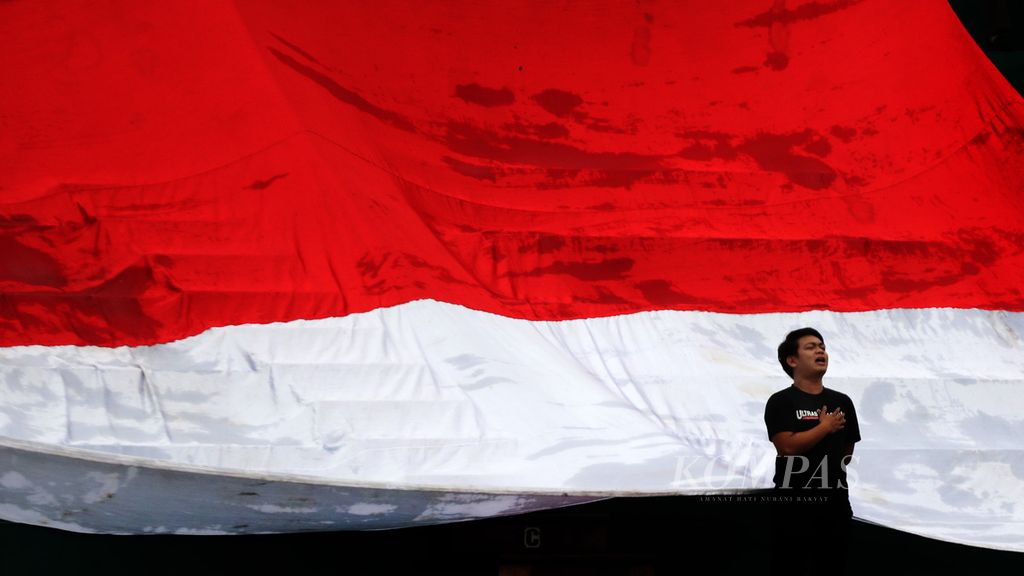 Suporter Indonesia berdiri di depan bendera Merah Putih raksasa yang dibentangkan pada laga terakhir Grup A cabang sepak bola SEA Games Vietnam 2021 antara tim nasional Indonesia dan Myanmar di Stadion Viet Tri, Phu Tho, Vietnam, Minggu (15/5/2022). 