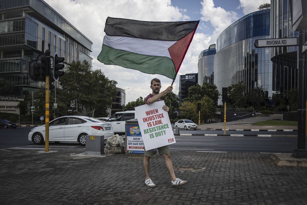 Aktivis pro-Palestina memegang spanduk dan membawa bendera Palestina saat berunjuk rasa menyusul keputusan Mahkamah Internasional (ICJ) atas kasus melawan Israel yang diajukan oleh Afrika Selatan di Den Haag di Konsulat AS di Johannesburg, Afrika Selatan, Jumat (26/1/2024). 