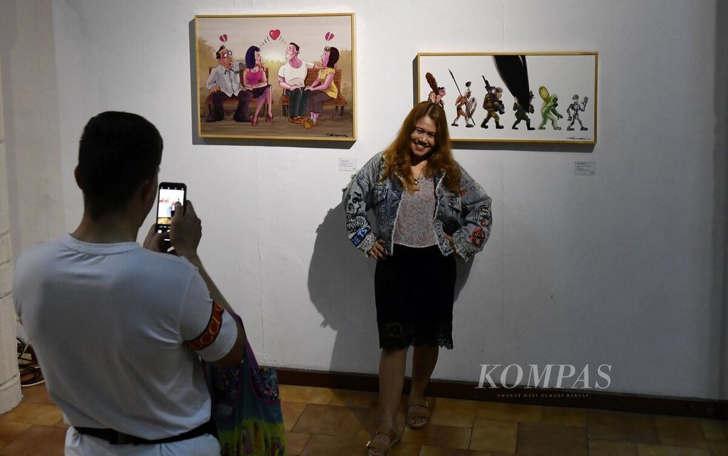 Pengunjung berfoto di depan karya yang dipamerkan dalam pameran kartun bertajuk "I Love U Gudbai" di Bentara Budaya Jakarta, Kamis (3/8/2023).