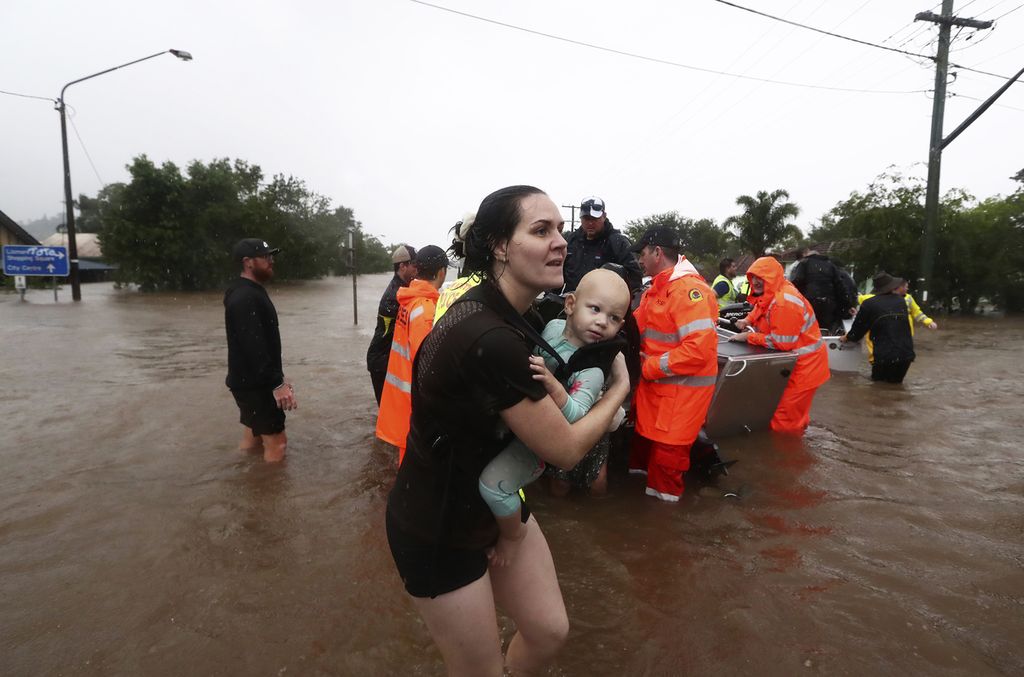 Seorang perempuan menggendong bayi saat warga menggunakan perahu untuk melewati banjir di Lismore, Australia, Senin (28/2/2022). Hujan deras menyebabkan banjir terparah di wilayah pesisir timur Australia. 