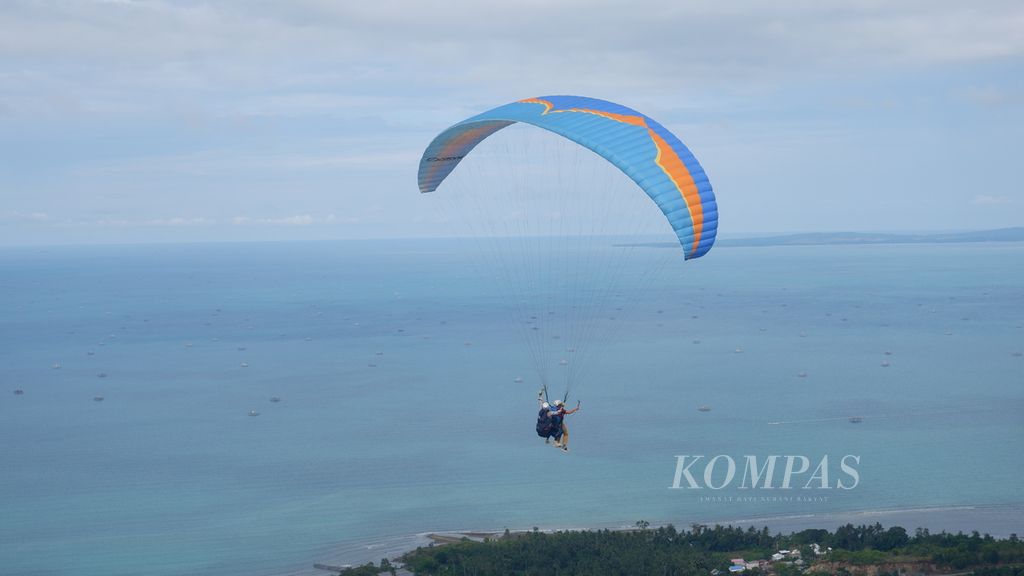 Terbang tandem paralayang dari puncak Bukit Bapake melintasi Desa Sarang Tiung, Kecamatan Pulau Laut Sigam, Kabupaten Kotabaru, Kalimantan Selatan, Kamis (7/7/2022). Di kawasan bukit tersebut mulai dikembangkan wisata olahraga udara (<i>aerosport</i>) paralayang dan gantole untuk pertama kalinya di Kalsel. 