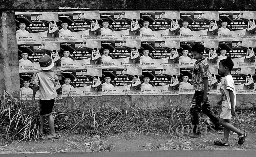 Anak-anak melintas di depan poster dari calon legislatif beserta partai, nomor urut dan janji kampanye di Duren Sawit, Jakarta Timur, Minggu (29/9). 