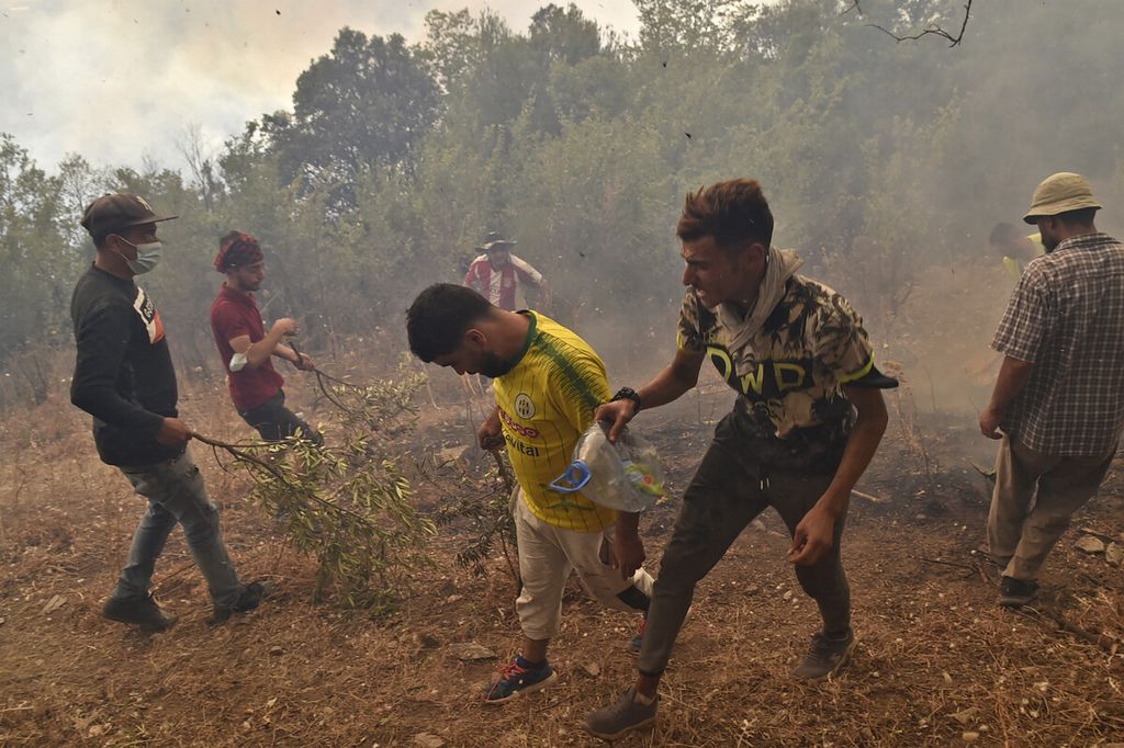 Sukarelawan, tanpa perlengkapan yang memadai, berusaha memadamkan api di hutan perbukitan di wilayah Kabylie, sebelah timur ibu kota Aljazair, Algiers, yang dilanda kebakaran, Kamis (12/8/2021). 
