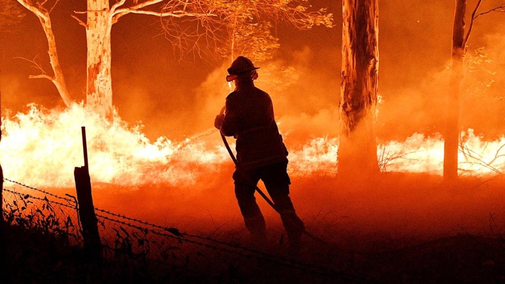 Foto yang diambil pada 31 Desember 2019 ini menunjukkan seorang petugas pemadam kebakaran menyemprot pohon dan bara api dalam upaya untuk mengamankan rumah-rumah di dekat kota Nowra di Negara Bagian New South Wales, Australia. Korban tewas akibat kebakaran hutan di New South Wales mencapai 15 orang.