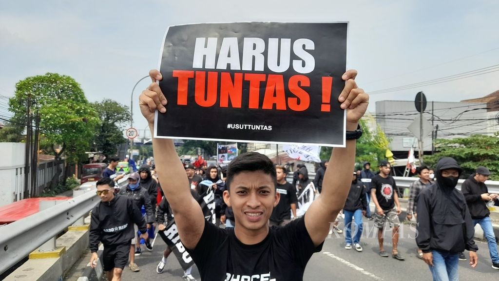 Seorang Aremania membentangkan poster Harus Tuntas saat menggelar aksi di Flyover Arjosari, Kota Malang, Jawa Timur, Minggu (20/11/2022), terkait kasus tragedi Kanjuruhan yang merenggut 135 nyawa dan lebih dari 600 orang lainnya luka-luka.