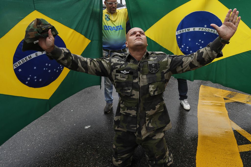 Seorang pendukung Presiden Brasil Jair Bolsonaro berlutut sambil membentangkan kedua tangannya di depan bendera Brasil dalam unjuk rasa menentang hasil pemilu Brasil di Rio de Janeiro, Brasil, 2 November 2022. 