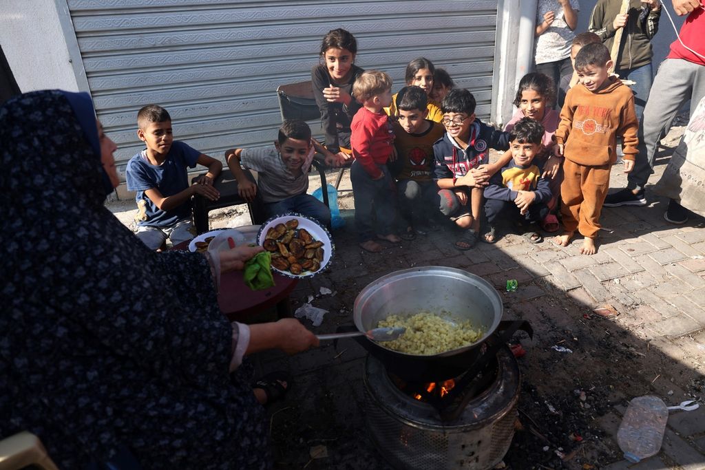 Seorang wanita memasak di atas api terbuka untuk anak-anak bersama keluarganya yang saat ini tinggal di toko keramik besar di Bureij, di tengah Jalur Gaza, Selasa (14/11/2023). 