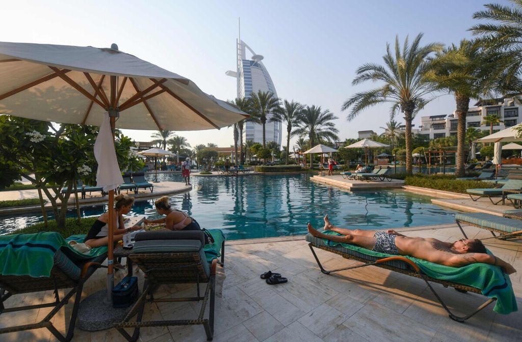 Beberapa wisatawan berjemur di tepi kolam renang di Hotel Al Naseem di Dubai, Uni Emirat Arab, 7 Juli 2020. Di latar belakangnya tampak Hotel Burj al-Arab. Dengan stiker bertulis "Selamat Datang" dan tes Covid-19 saat kedatangan, Dubai kembali membuka industri pariwisatanya untuk para pelancong internasional. (Photo by KARIM SAHIB / AFP)