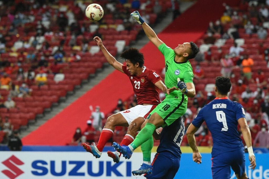 Kiper timnas Singapura. Hassan Sunny (tengah), mencoba menghalau bola saat beradu dengan pemain timnas Indonesia, Hanis Saghara Putra, pada laga kedua semifinal Piala AFF Suzuki 2020 di Stadion Nasional, Singapura, 25 Desember 2021.