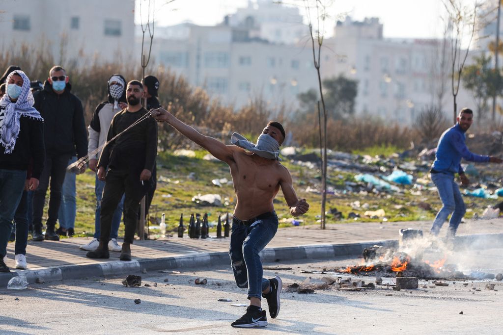 Seorang warga Palestina melempari militer Israel dengan batu di tengah kepungan gas air mata saat bentrokan di Ramallah, Kamis (26/1/2023).