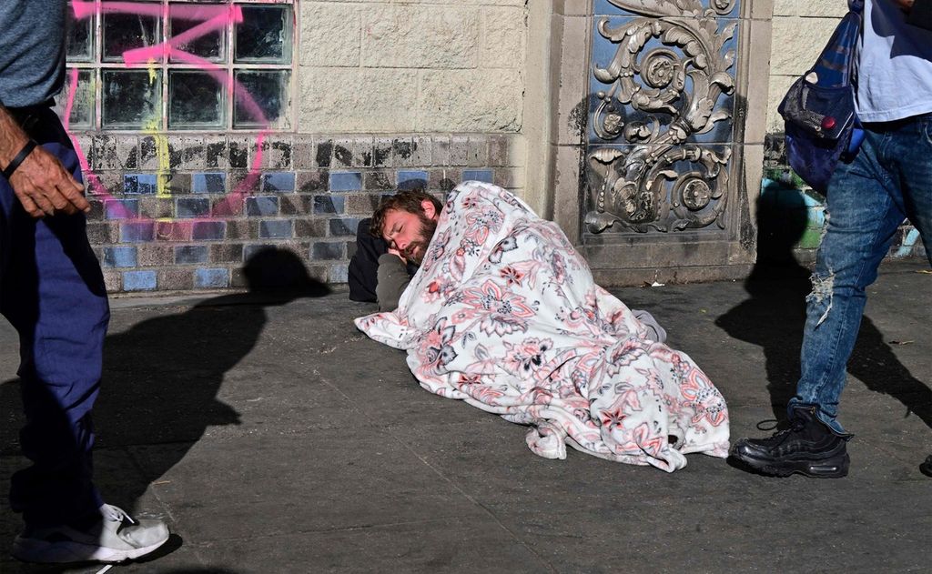 Para pejalan kaki melintas di depan tunawisma yang tengah tidur di trotoar di Los Angeles, California, Rabu (22/11/2023).