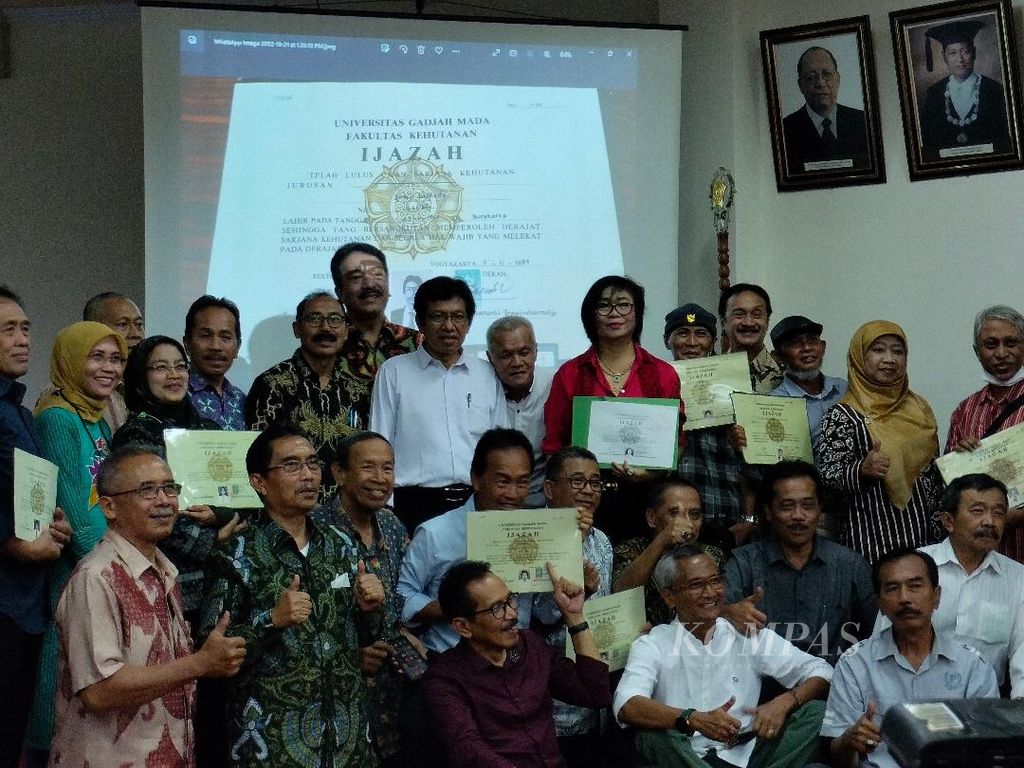 Alumni mahasiswa Fakultas Kehutanan Universitas Gadjah Mada, Yogyakarta, berfoto bersama dengan menampilkan ijazah masing-masing dengan berlatar belakang foto ijazah Presiden Joko Widodo, Jumat (21/10/2022).