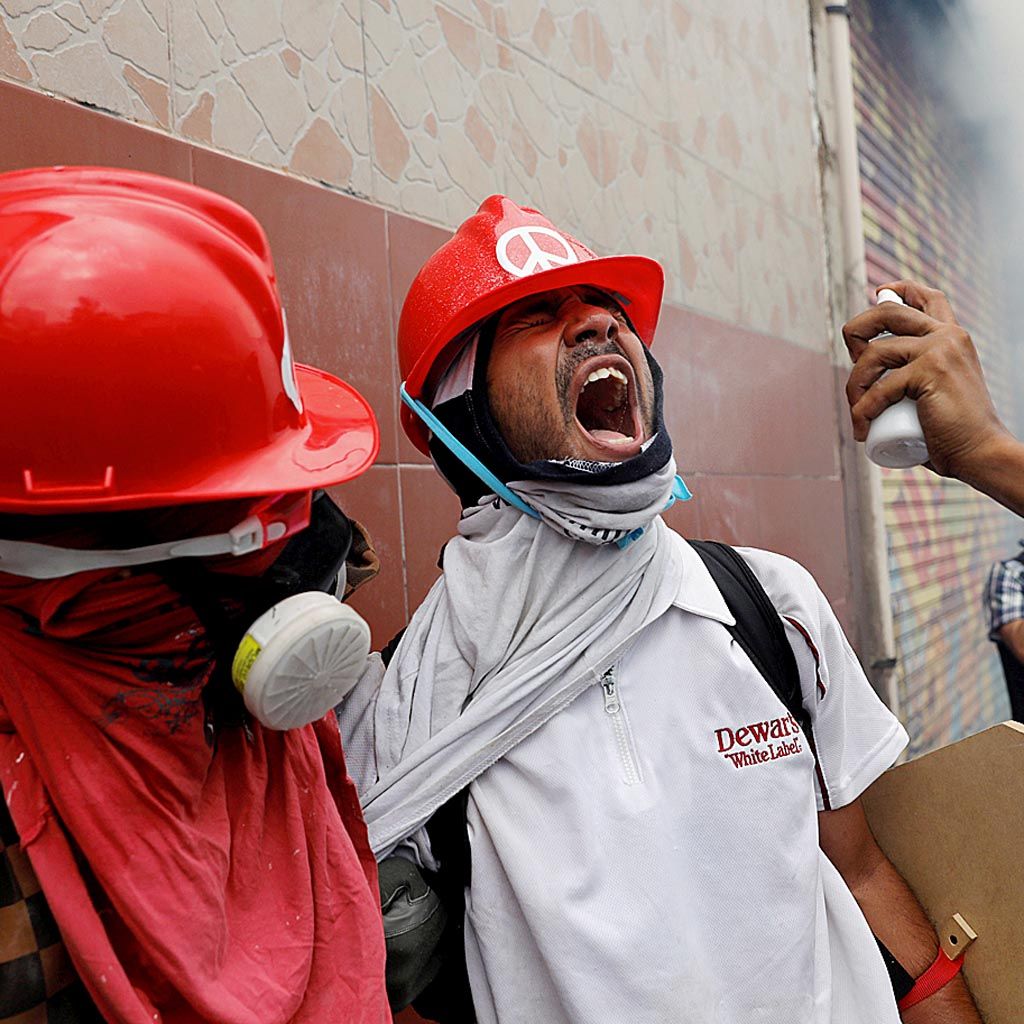 Pengunjuk rasa berusaha mengatasi dampak gas air mata di sela-sela bentrok dengan polisi anti huru-hara dalam unjuk rasa menentang Presiden Nicolas Maduro di Caracas, Venezuela, Rabu (3/5). 