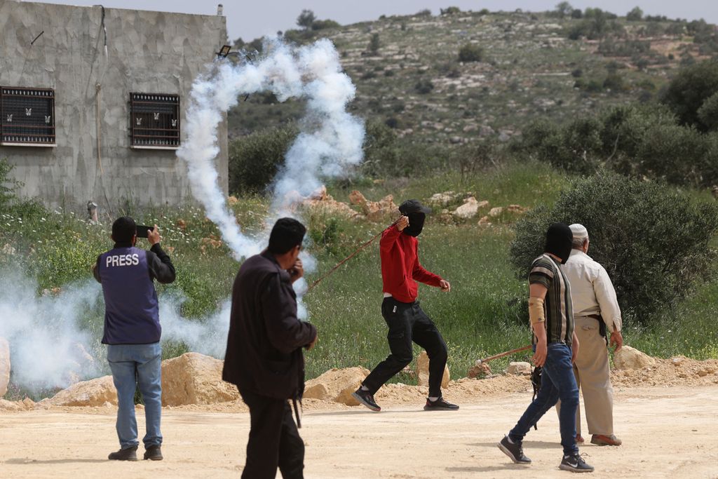 Warga Palestina melemparkan balik kaleng gas air mata yang ditembakkan aparat Israel dalam unjuk rasa di Nablus, Tepi Barat, pada April 2023. 