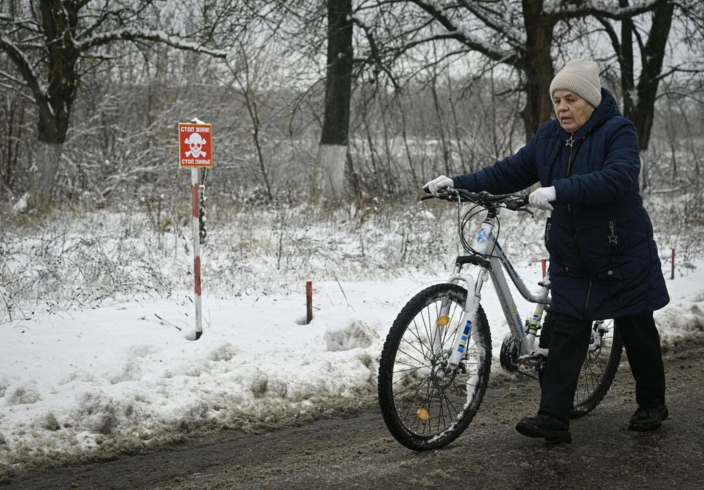 Seorang perempuan mendorong sepeda melewati jalan dengan tanda "Awas Ranjau" di dekat Desa Makariv, sebelah barat Kyiv, Ukraina, 22 November 2022, di tengah invasi Rusia. 