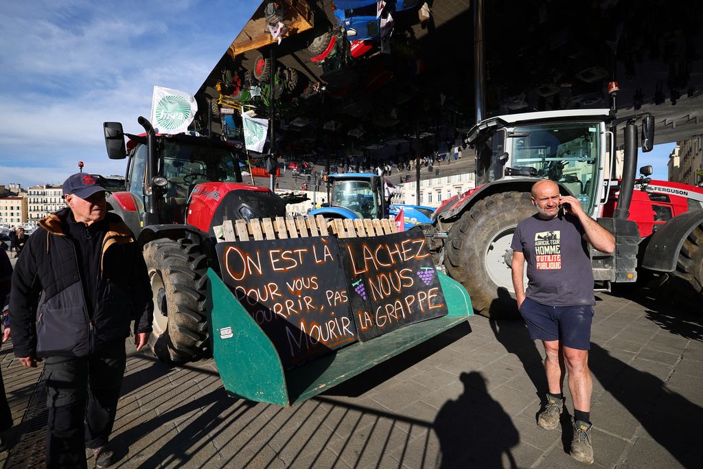 Seorang petani (kanan) di depan traktor bertuliskan "Kami di sini untuk memberi makan Anda, jangan mati, berhenti mengganggu kami" di bawah Ombirere di Pelabuhan Vieux (Pelabuhan Tua) dalam demonstrasi petani Perancis menentang kebijakan pertanian di Marseille, Perancis. 