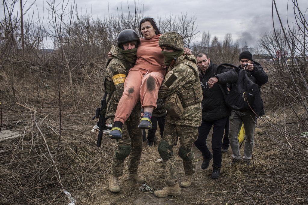 Seorang perempuan warga Ukraina digotong oleh dua anggota militer Ukraina melintasi jalan setapak saat mencoba keluar dari Irpin, tidak jauh dari ibu kota Ukraina Kiev, Minggu (6/3/2022).