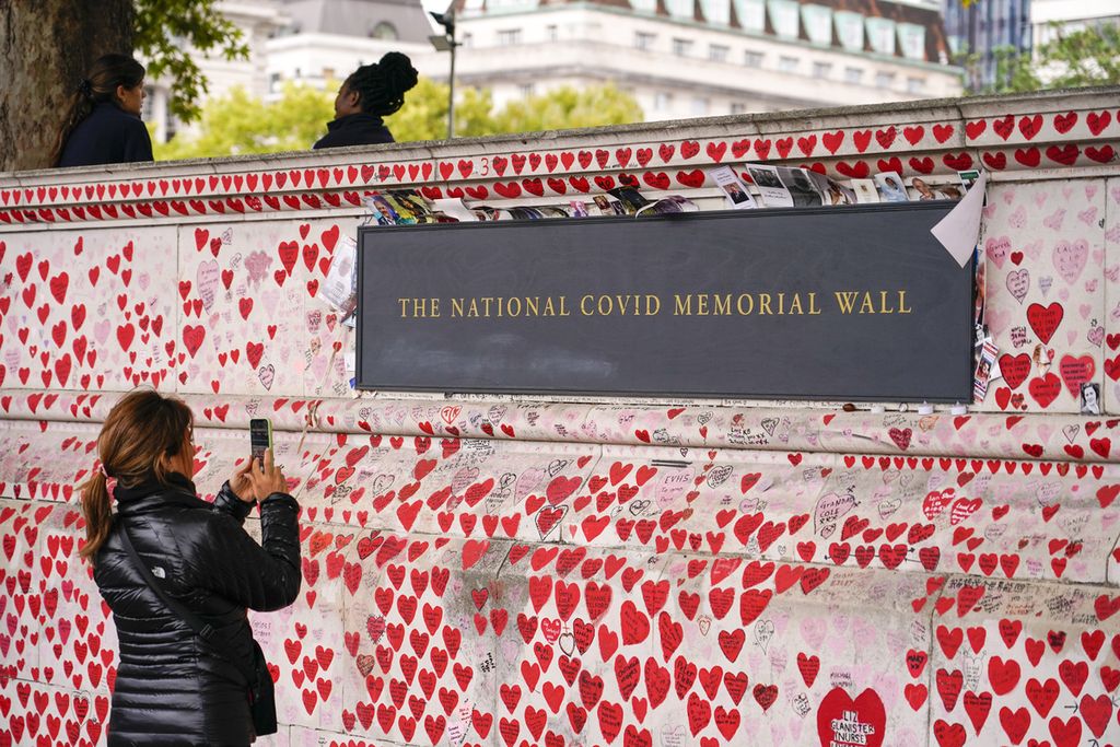 Seorang perempuan mengambil gambar National Covid Memorial Wall di tepi Sungai Thames bagian selatan di London, Inggris, 4 Oktober 2022. Kasus Covid-19 di Inggris dan Uni Eropa naik lagi menjelang musim dingin. 