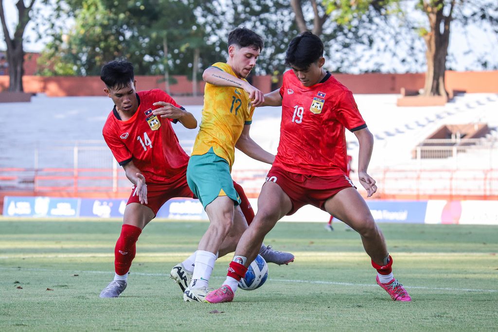 Pemain Australia, Jake Najdovski (tengah), berusaha melewati hadangan pemain Laos, Phousomboun Panyavong (kanan) dan Phetvixay Phimmasen (kiri), pada pertandingan penyisihan Grup B Piala AFF U-19 di Stadion Gelora 10 November, Surabaya, Kamis (18/7/2024). Australia menang 6-0. 