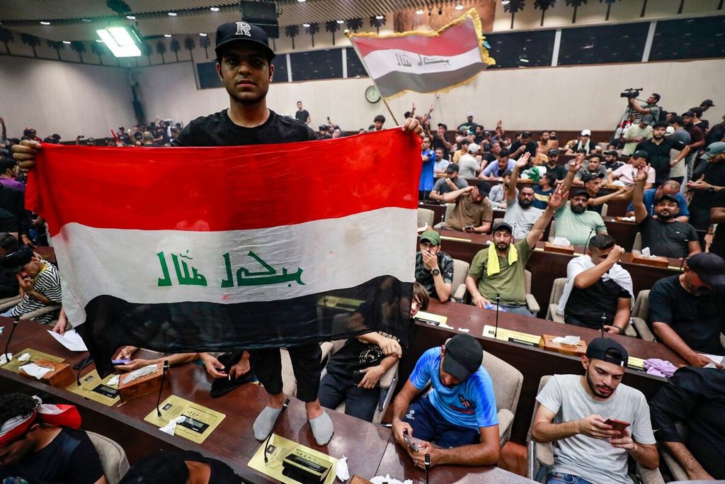 Seorang pria berdiri di atas meja di dalam gedung parlemen Irak, sambil membentangkan bendera Irak, di tengah aksi pendudukan gedung parlemen oleh para pendukung ulama Irak, Moqtada al-Sadr, di area Zona Hijau, Baghdad, Irak, Sabtu (30/7/2022). 