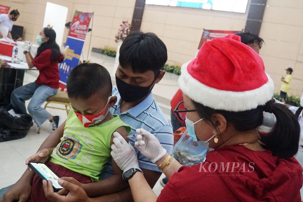 Narendra (7) disuntik vaksin Covid-19 sambil bermain gim ponsel di pangkuan ayahnya, Rabu (15/12/2021), di Graha Gubernuran, Manado, Sulawesi Utara.