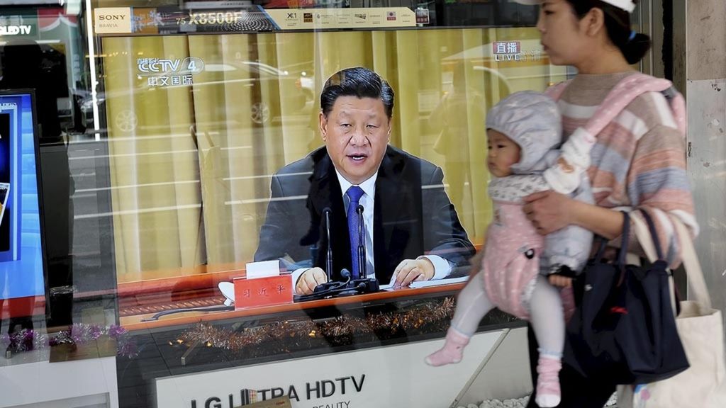 Seorang ibu sambil menggendong anaknya berjalan melewati sebuah toko di Kota New Taipei, Rabu (2/1/2019), yang memajang sebuah televisi yang tengah menayangkan pidato resmi Presiden China Xi Jinping. Xi berpidato untuk memperingati 40 tahun pesan yang dikirim ke Taiwan pada 1979.