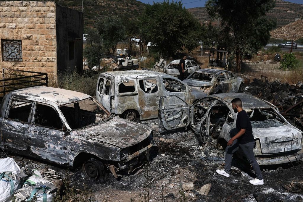 Seorang pria berjalan di dekat puing mobil-mobil yang dibakar, diduga oleh para pemukim Israel, di Al-Lubban Al-Gharbi, wilayah pendudukan Tepi Barat, Rabu (21/6/2023). 