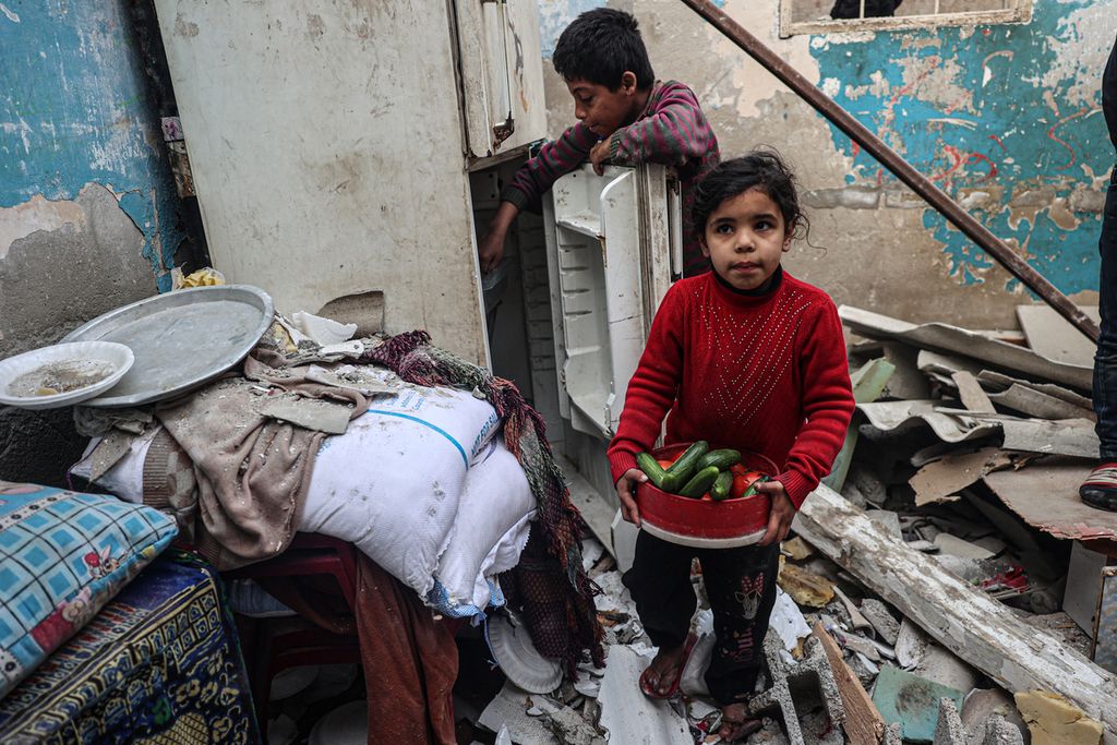 Seorang anak membawa makanan dari rumahnya yang rusak akibat pengeboman Israel di Rafah, Minggu (25/2/2024). 