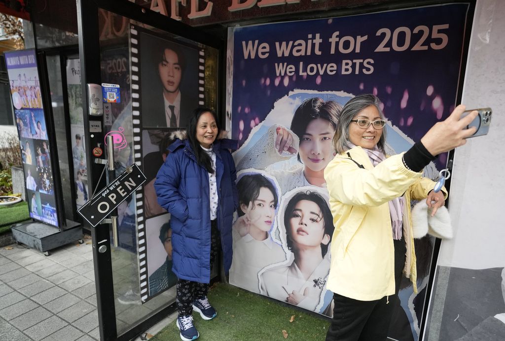 Seorang wanita berswafoto dengan gambar anggota band <i>K-pop</i> BTS di depan kafe di Seoul, Korea Selatan, Senin (11/12/2023).
