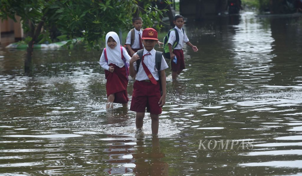 Siswa SD Negeri Banjarasri melewati banjir yang menggenang halaman sekolah mereka saat akan pulang, Kecamatan Tanggulangin, Kabupaten Sidoarjo, Jawa Timur, Selasa (11/2/2020). 