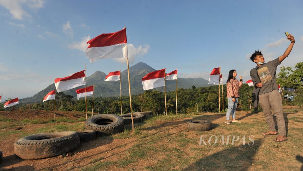 Wisawatan berfoto bersama bendera merah putih dengan latar belakang Gunung Penanggungan di objek wisata Potoek Suko, Kecamatan Trawas, Kabupaten Mojokerto, Jawa Timur, Sabtu (15/8/2020). 