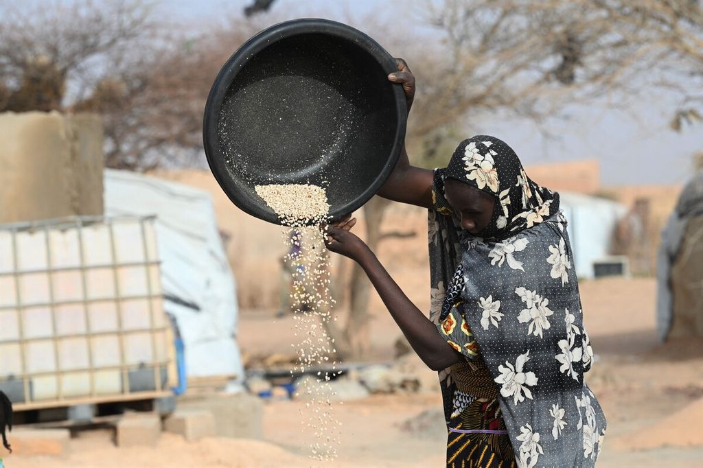 Seorang perempuan menuangkan bahan makanan berbentuk biji-bijian ke sebuah wadah di sebuah kamp pengungsian di Quallam, Niger, pada 3 Mei 2022. Kenaikan bahan makanan telah semakin membebani warga di dunia, terutama warga ekonomi kelas bawah.  
