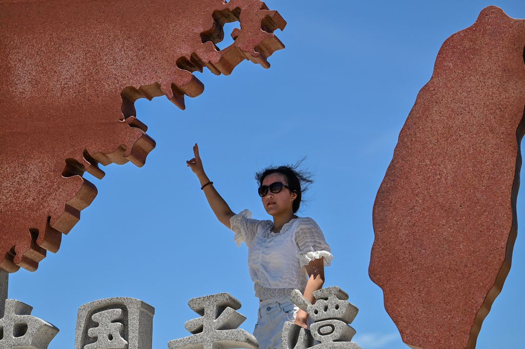 Seorang wisatawan berpose di monumen yang menggambarkan China daratan (kiri) dan Taiwan (kanan) di Pulau Pingtan, 6 Agustus 2022. 