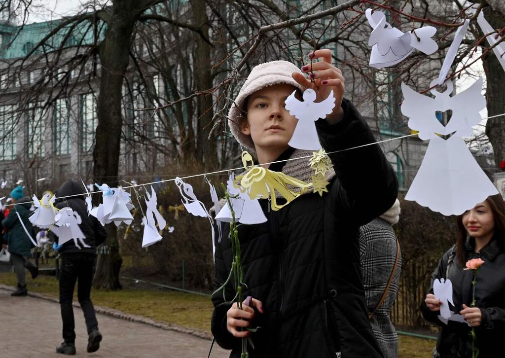 Seorang perempuan memasang kertas-kertas putih untuk mengenang orang-orang yang meninggal dalam demonstrasi anti-pemerintah pada tahun 2014 di taman untuk mengenang para aktivis Maidan di dekat Lapangan Kemerdekaan, Kiev, Ukraina, 18 Februari 2022. 