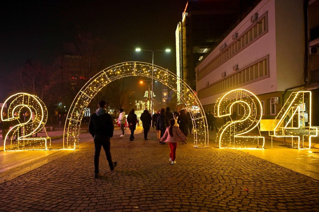 Para pejalan kaki melewati tulisan berlampu 2024 yang dipajang di pusat kota Pristina, Kosovo, Sabtu (30/12/2023). 