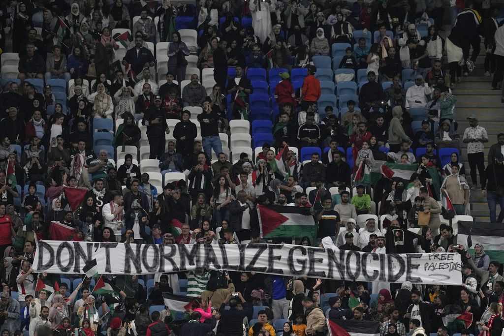 Para penonton membentangkan spanduk dengan pesan berbahasa Inggris, "Jangan Normalisasi Genosida", pada laga Palestina melawan UEA, Kamis (18/1/2024). 