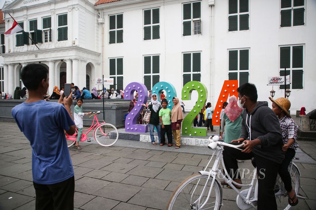 Pengunjung berfoto dengan latar belakang ornamen tahun 2024 di Taman Fatahillah, Jakarta Barat, Selasa (26/12/2023). Pada masa libur Natal dan Tahun Baru 2024, kawasan Kota Tua dipadati pengunjung dari daerah-daerah. 