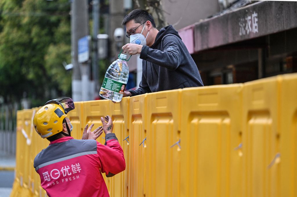 Seorang warga Shanghai menerima segalon air mineral dari seorang petugas jasa antar pada 30 Maret 2022.