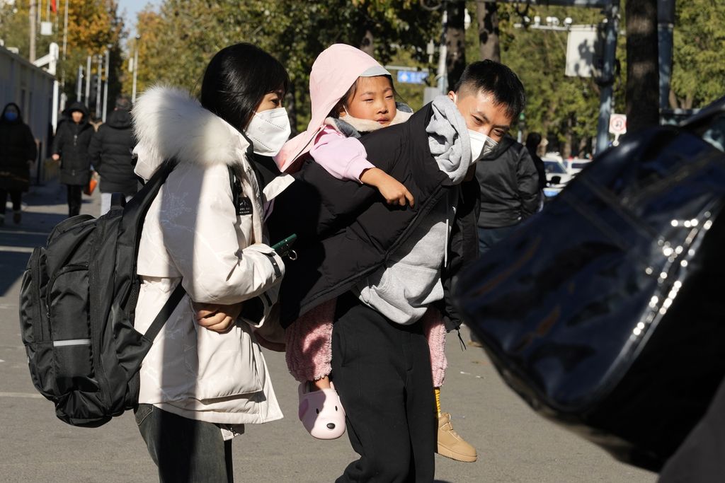 Pria menggendong seorang anak saat mereka meninggalkan rumah sakit anak-anak di Beijing, Jumat (24/11/2023). Pejabat Tiongkok mengatakan, mereka tidak mendeteksi adanya penyakit yang tidak biasa atau baru terkait lonjakan penyakit pernapasan di China, terutama pada anak-anak.