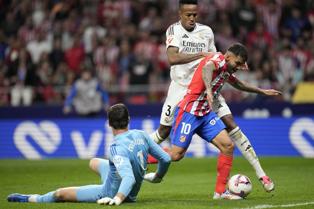 Penyerang Atletico Madrid Angel Correa melewati kiper Real Madrid Thibaut Courtois dan bek Eder Militao untuk mencetak gol penyama kedudukan saat derbi Madrid di Stadion Metropolitano, Senin (30/9/2024) dini hari WIB. Laga yang diwarnai kericuhan penonton ini berakhir imbang 1-1.